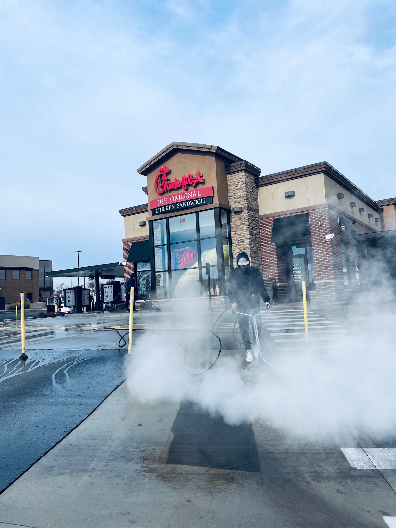 Hot water pressure washing surface cleaner blasting away oil and grime during drive thru power washing service